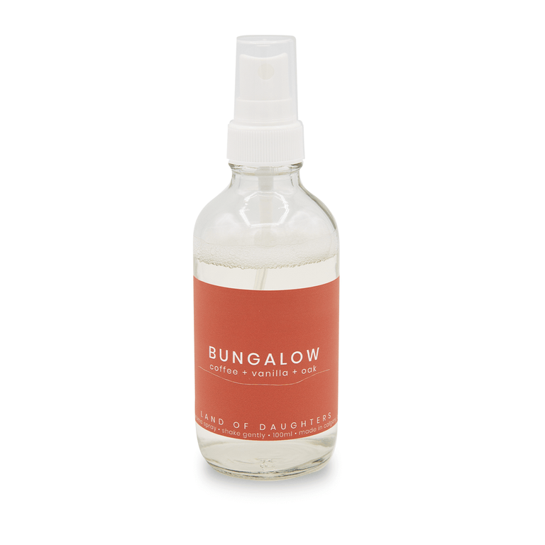 Glass aroma spray bottle filled with liquid with a burnt orange label reading Bungalow, coffee + vanilla + oak on a white background